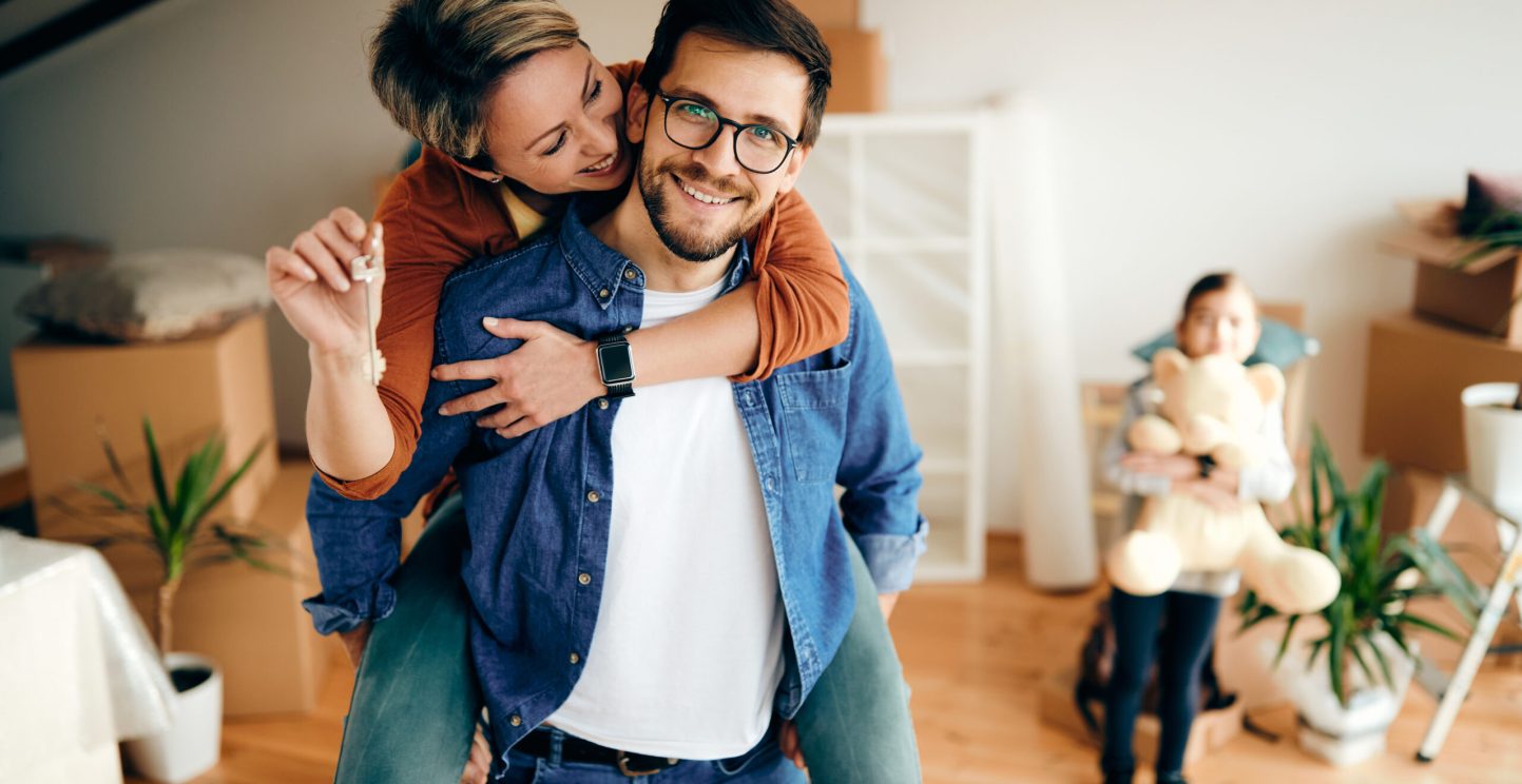 Happy mid adult couple having fun while relocating into a new house. Their daughter is in the background.